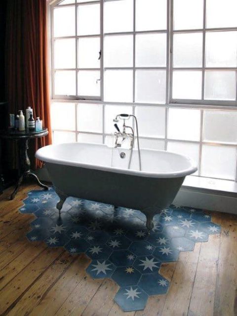 a chic bathroom with a laminate to blue hex tile floor, a vintage clawfoot tub and a side table