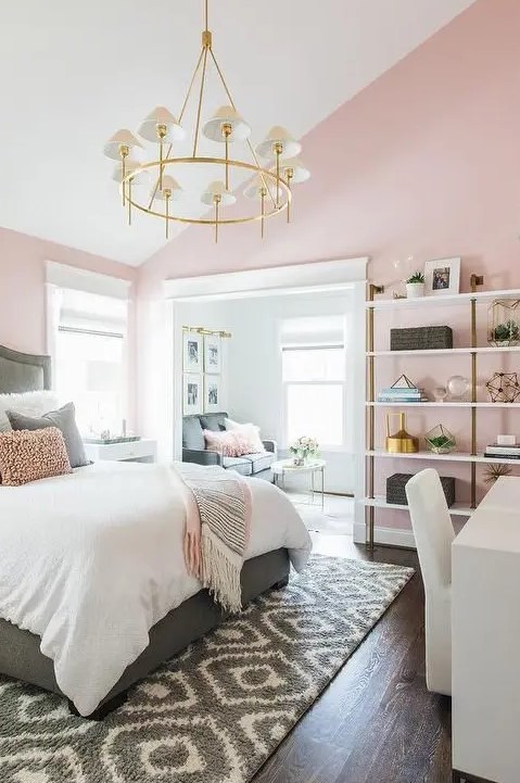 a chic bedroom with pink walls,a grey bed with neutral bedding, a shelving unit, a white desk and a chair, a glam chandelier