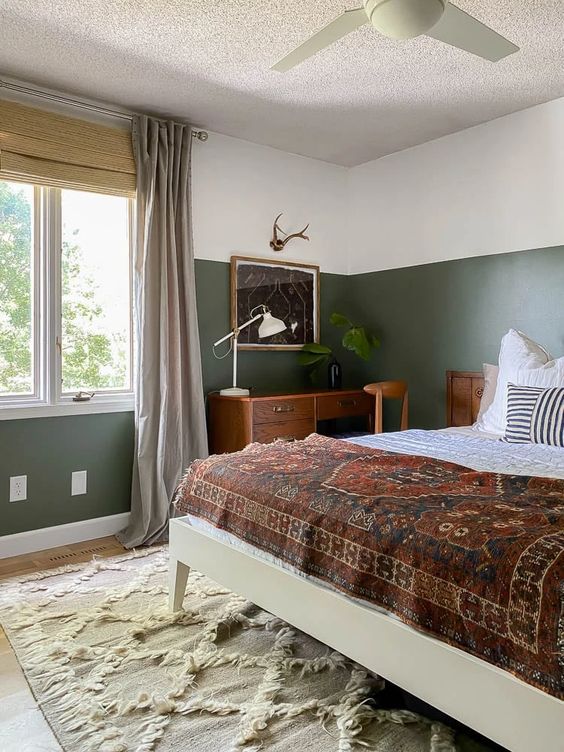 a cozy modern bedroom with color block walls, a large bed with printed bedding, a stained desk and a chair, some plants
