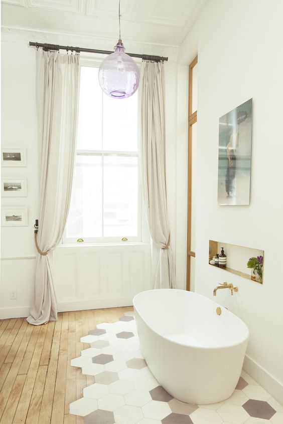 a cozy neutral bathroom with a laminate to hex tile floor, an oval tub, a niche shelf and neutral curtains are a cool combo