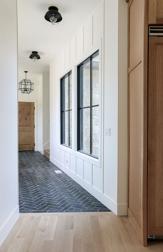 a hallway clad with black herringbone tiles transitioning into light-stained laminate without any borders for a modern feel