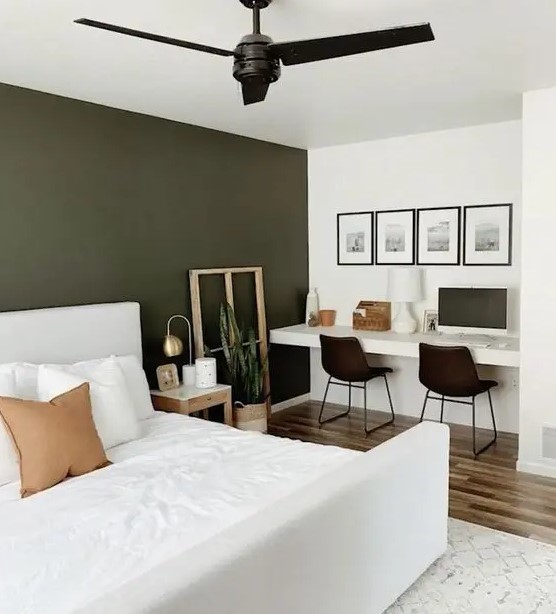 a lovely and functional bedroom with an olive green accent wall, a white bed with bedding, built-in desk, black chairs and a gallery wall