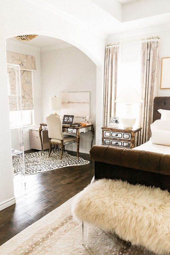 a luxurious bedroom with an alcove home office, a refined vintage desk and a chair, an acrylic stand, a brown bed, a faux fur bench