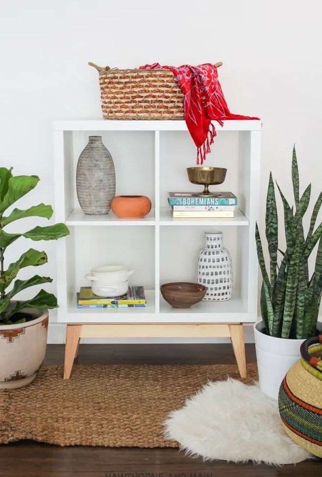 a mid-century modern storage unit of a Kallax shelf placed on wooden legs, with lovely decor and potted plants around