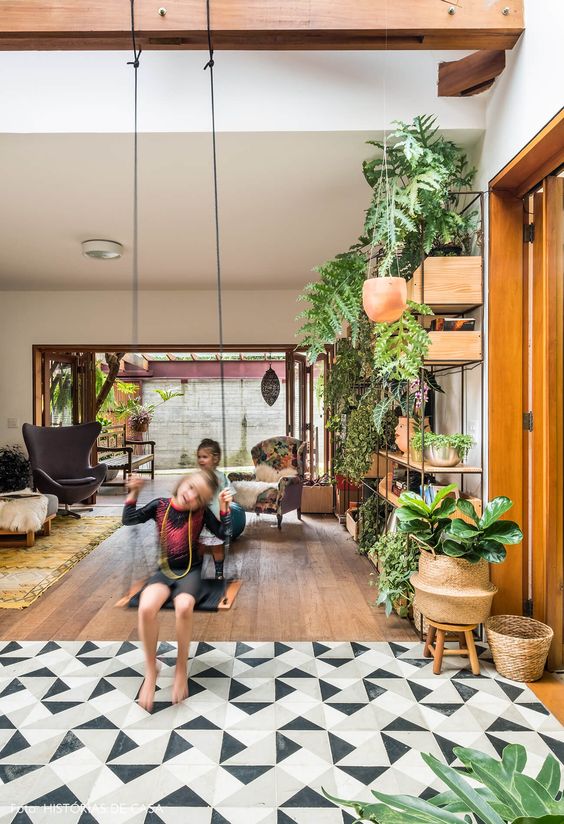 a modern boho space with a floor transition from laminate to geo tiles, a large shelving unit with potted plants and a swing