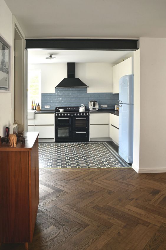 a modern kitchen with white cabinets and a blue tile backsplash, a tiled floor and a parquet floor in the next zone