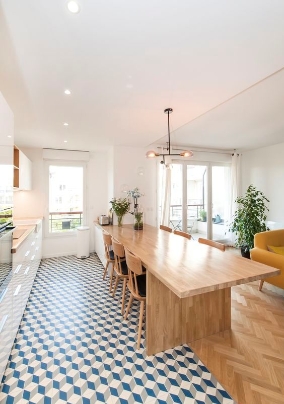 a modern space with white kitchen cabinetry, a large table and chairs, a tiled floor and a parquet one in the living room