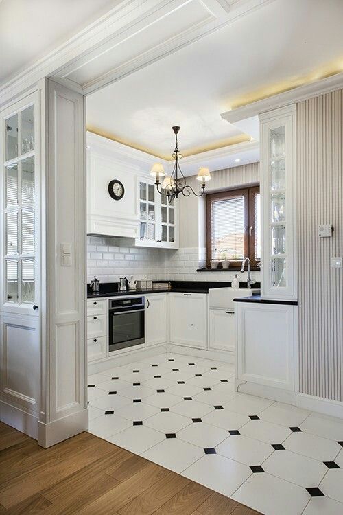 a modern white kitchen with black countertops, a white subway tile backsplash, a black and white tile floor and a laminate floor in the next zone