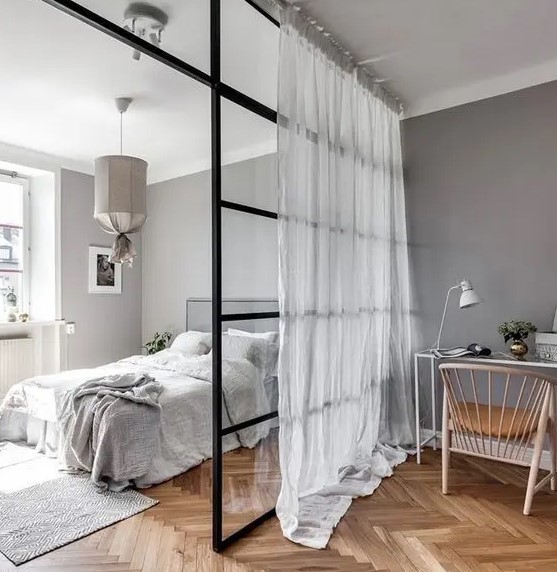 a pretty Scandinavian bedroom in shades of grey, with a glass space divider for a home office nook is a functional idea
