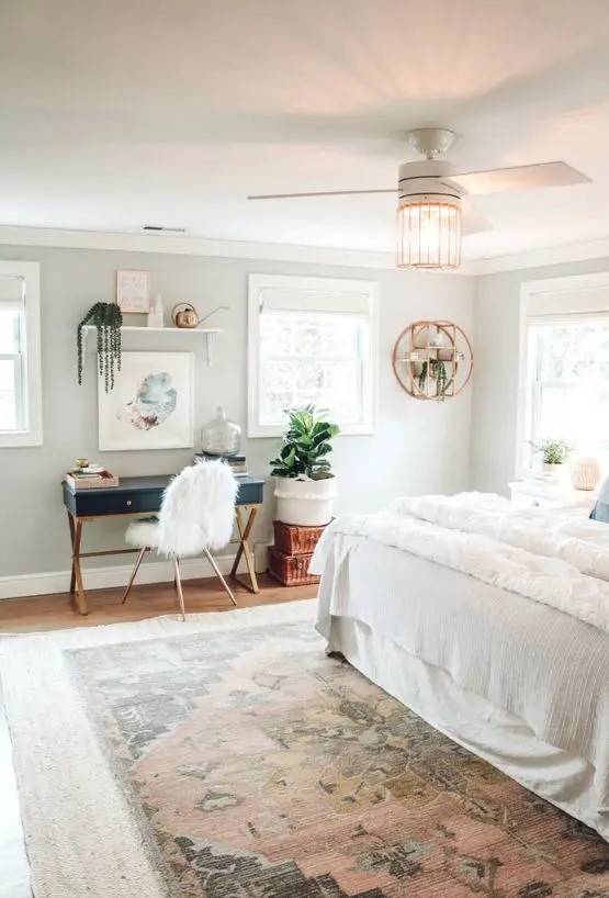 a pretty boho bedroom with a navy desk and a faux fur chair, a floating shelf and potted plants, neutral bedding and a printed rug