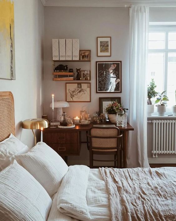 a pretty boho bedroom with a stained desk in the corner, a cane chair, a gallery wall, a bed with a cane headboard and neutral bedding