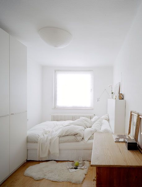 a small and airy white bedroom with a low bed and neutral bedding, a wardrobe, a stained desk and some simple decor