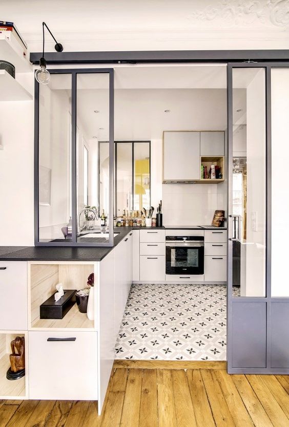 a small white kitchen with black countertops, sliding doors, a printed tile floor that transitions into laminate flooring