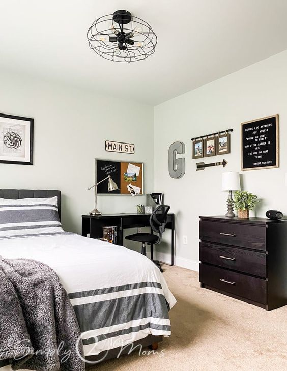 a stylish bedroom with a grey bed and printed bedding, a black desk and a chair, a dark-stained dresser and some decor