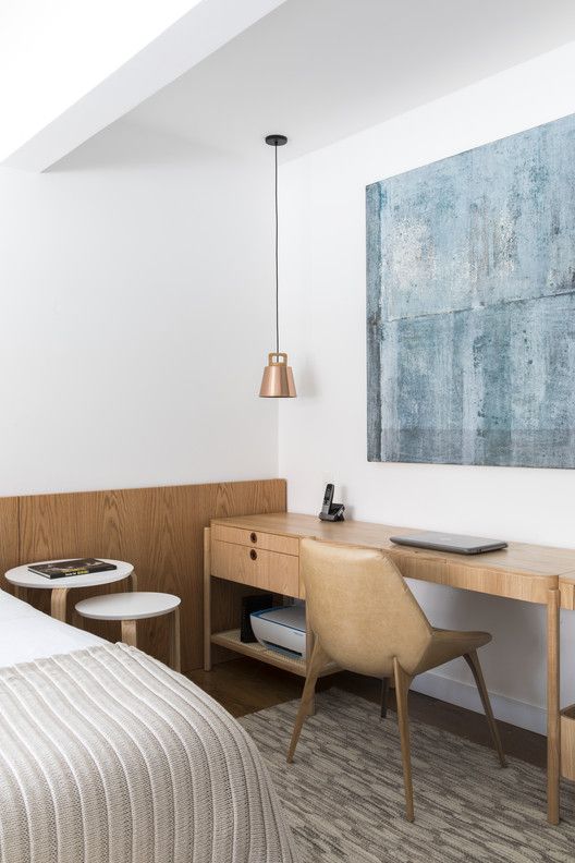 a stylish minimal bedroom with a bed and neutral bedding, a couple of nightstands, a long and narrow desk and a leather chair