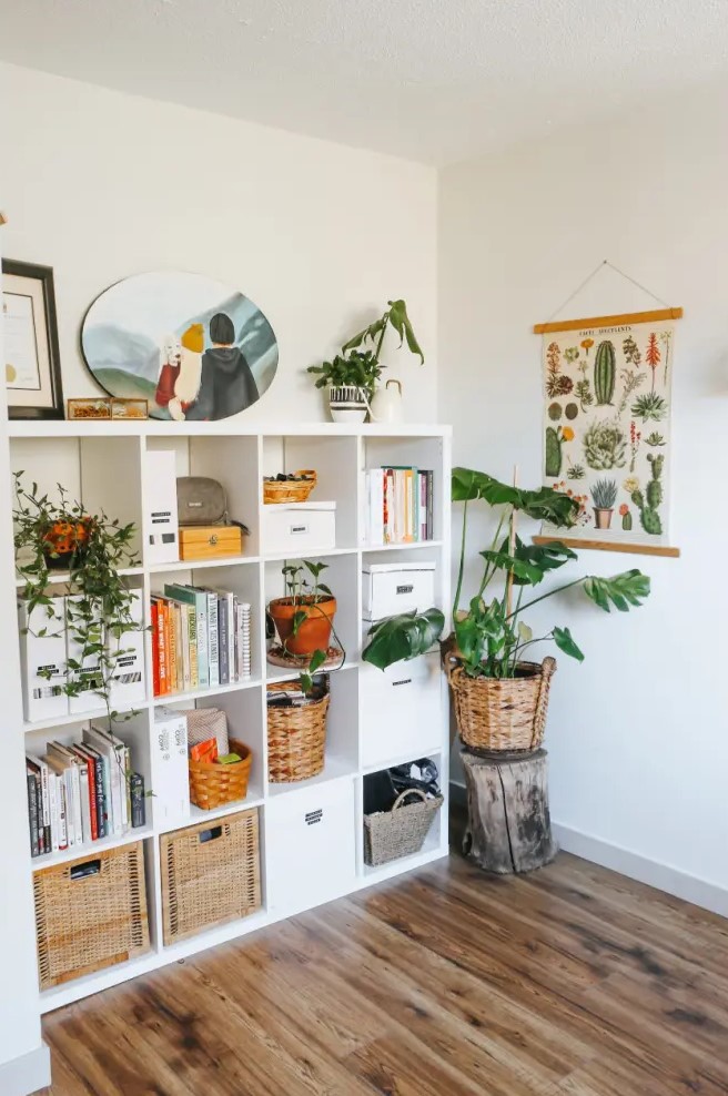 an IKEA kallax unit used as a bookshelf, finished with woven and usual box drawers, with potted greenery and cool decor