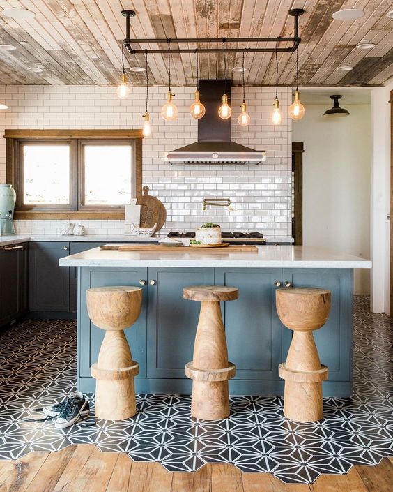 an eye-catchy kitchen with blue cabinetry, a kitchen island, cork stools, a floor transition with black and white tiles and laminate