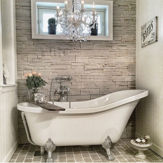 faux stone works as a perfect backdrop for a claw foot tub and a refined chandelier