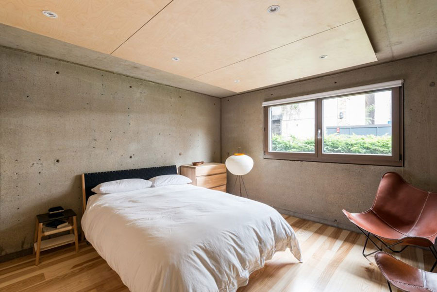The guest bedroom is decorated with concrete and warm colored wood, it's very laconic