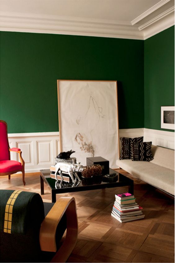 super bold space with works of art and white wainscoting to highlight the bold green color of the walls and a red chair