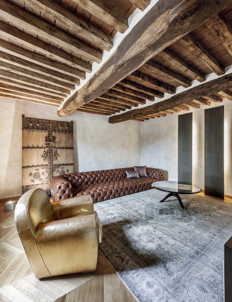 A faded vintage rug, a large leather sofa and a gold chair look stunningly harmonious together