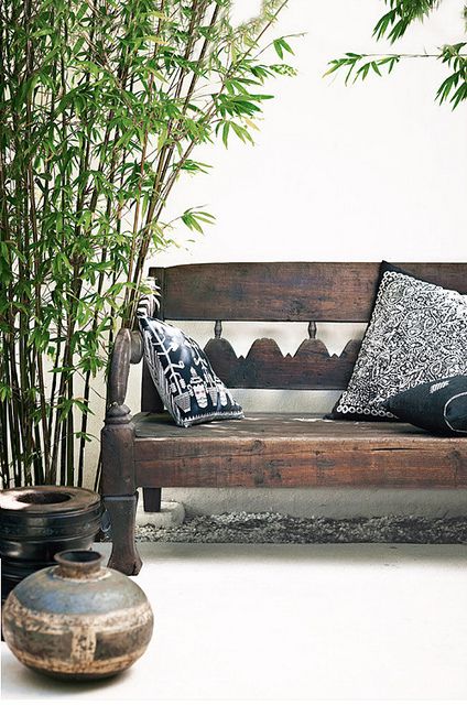 a worn carved dark wood bench with dark pottery for outdoors