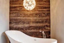 21 worn wood wall contrasts with a modern bathtub and chandelier