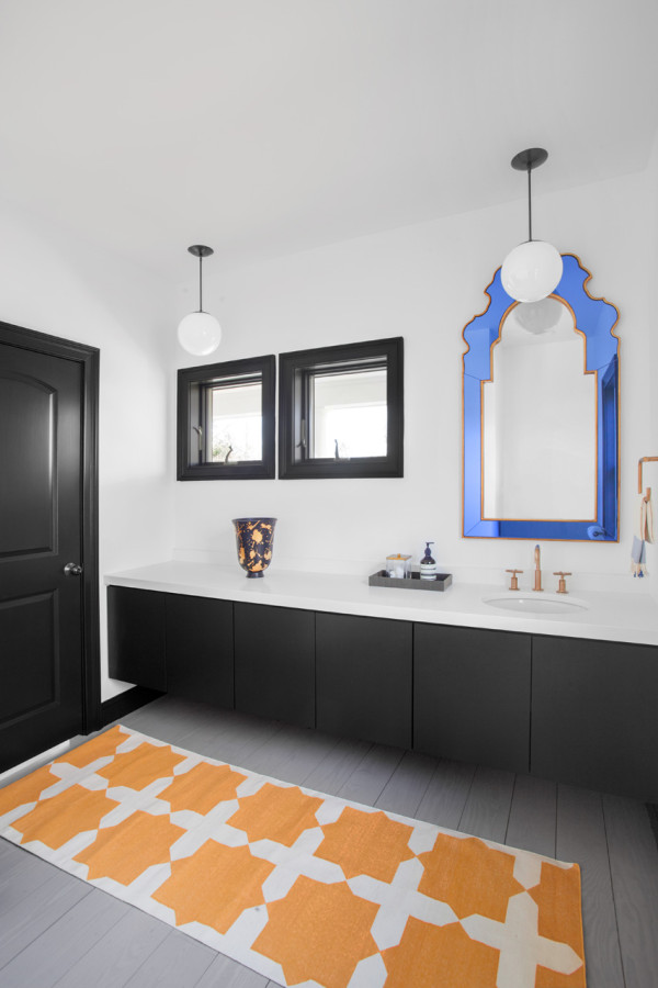 Black and white bathroom is spruced up with a whimsy blue frame mirror and an orange patterned rug