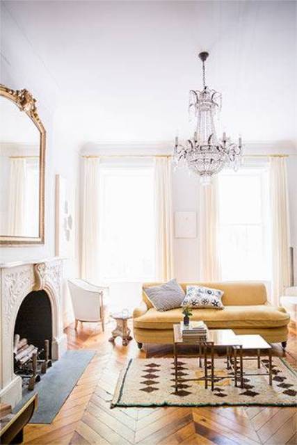 The living room is vintage in warm shades like ocher and buttermilk. A refined chandelier, vintage fireplace and mirror create an ambience