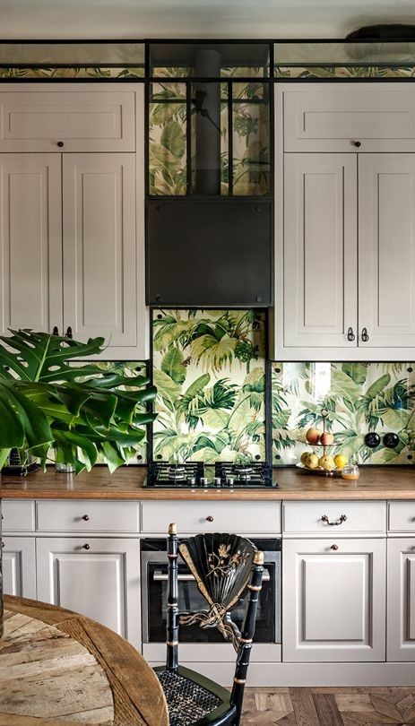 The kitchen mixes traditional cabinets, botanical wallpaper and natural wooden furniture