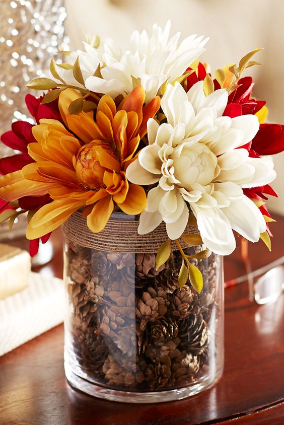 arrangement of faux dahlias, complete with a glass vase filled with pinecones