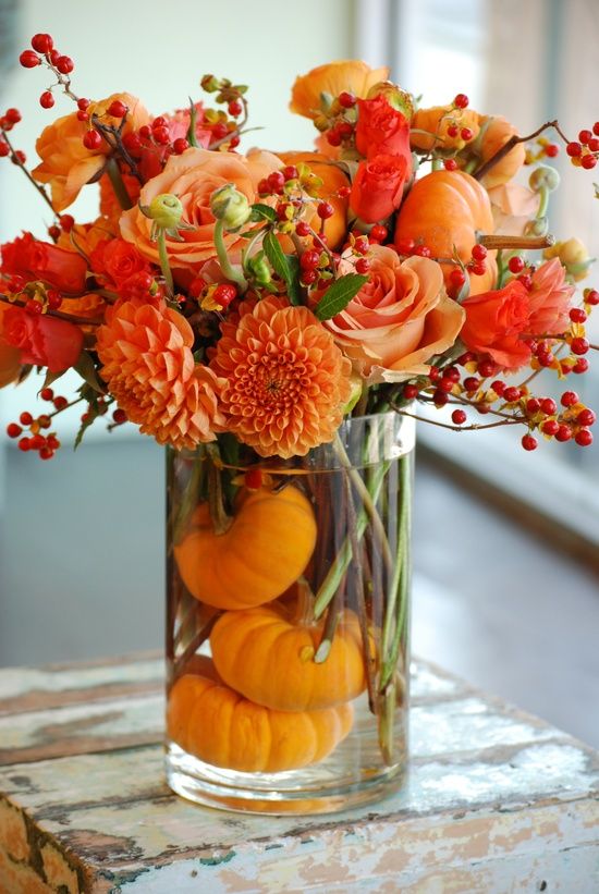 orange dahlias, roses, berries and pumpkins inside the glass vase