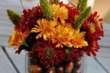19 acorns put into a glass vase and a bold floral arrangement over them