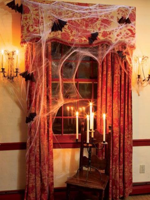 Halloween window decor with faux spiderweb, bats and a vintage candle holder