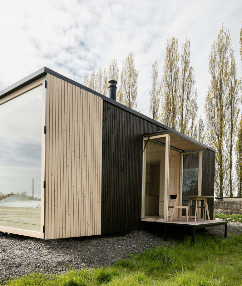 The house is clad with dark wood outside, and there's a small terrace with a small dining area