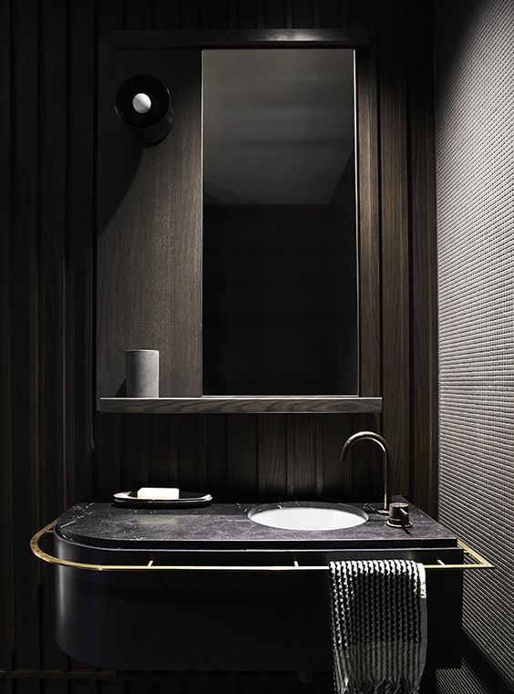 modern bathroom space with dark wood panels, a black marble counter and a large mirror