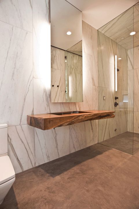 a stone slab and a rough wood countertop highlighted with lights behind the mirror