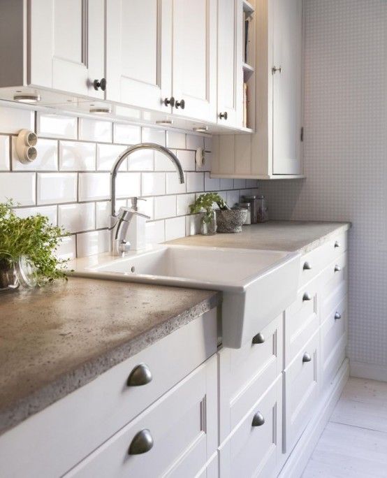 a chic modern white Scandinavian kitchen with white subway tiles and concrete countertops plus potted greenery