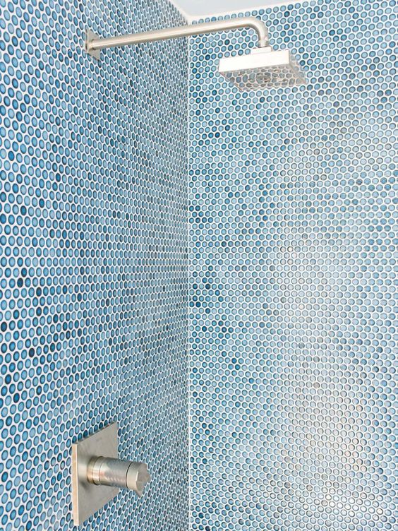 the sharp angles of the shower head and water valve offers a sleek look and contrasts with the penny round tiles on the shower walls