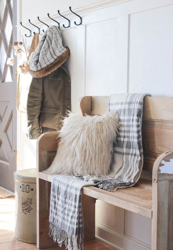 simple farmhouse entryway is perfectly decorated for winter with large coat hooks, a rustic bench, and a place for snow-covered boots