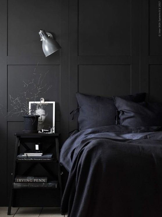 a chic Nordic moody bedroom with black paneling, navy bedding and black furniture plus a sconce