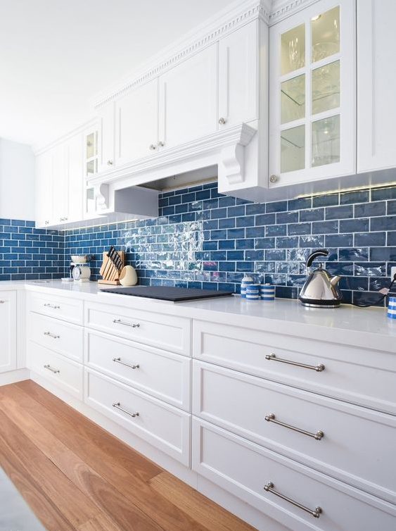 a cozy coastal kitchen in white, with bold blue subway tiles that add color and hint on the location