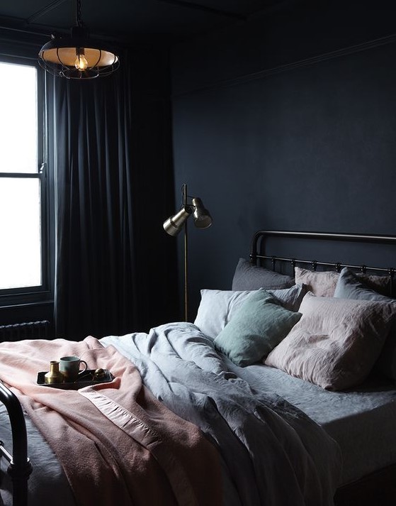 a dark minimalist bedroom with a metal bed, a floor and a pendant lamp, pastel bedding and dak curtains