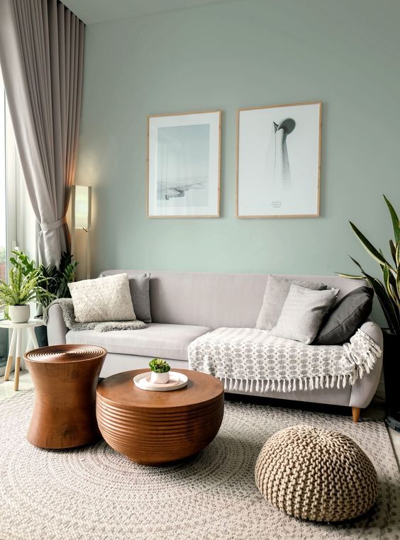 a delicate living room with light green walls, a greige sofa and neutral pillows, stained wooden tables and greige curtains