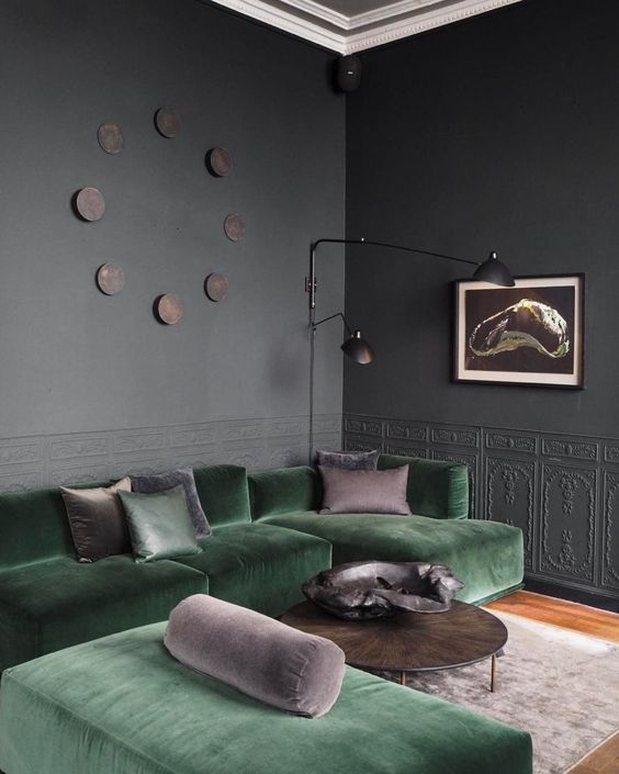a graphite grey living room with molding, a green sectional and a daybed, some taupe pillows, a coffee table and black lamps