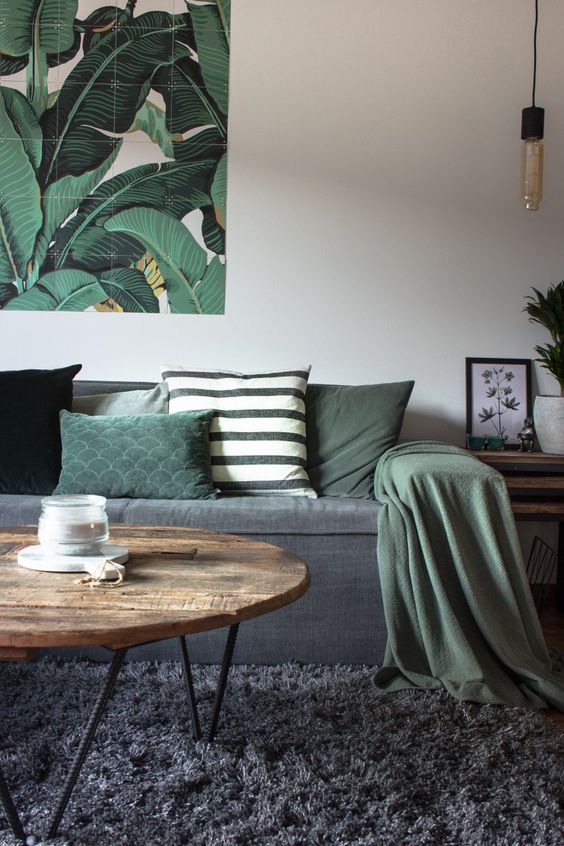 a lovely living room with a graphite grey sofa and rug, green pillows and a blanket, a bold artwork, a coffee table and a pendant lamp