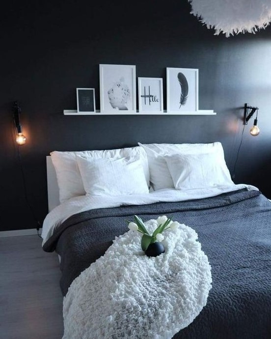 a minimal bedroom with a black accent wall, a ledge with artworks, a fluffy lamp and black and white bedding