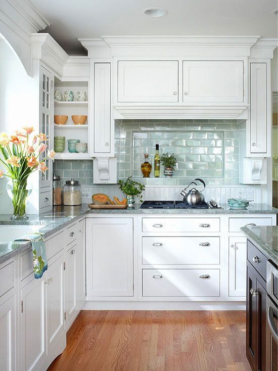 a modern white kitchen with a green subway tile backsplash, a grey stone countertop and silver fixtures