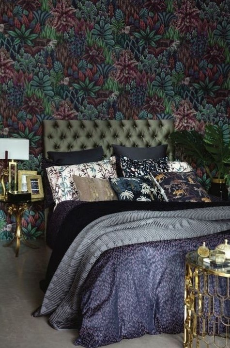 a moody and refined maximalist bedroom with a dark floral wall, a green upholstered bed, printed bedding, gilded touches for more elegance