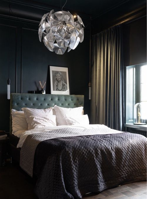 a moody bedroom with black walls and a ceiling, a green upholstered bed, neutral bedding, a catchy pendant lamp and chic curtains